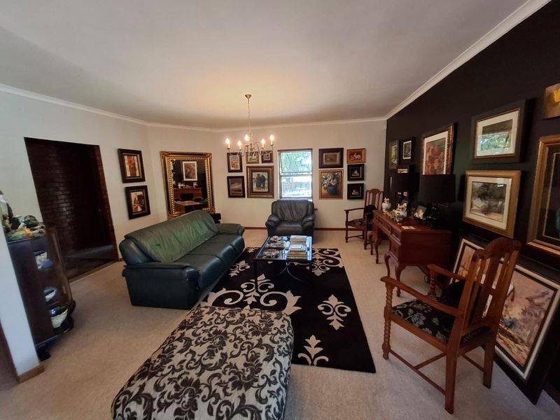 A spacious living room featuring neutral carpeting, a central chandelier, and a striking dark accent wall.