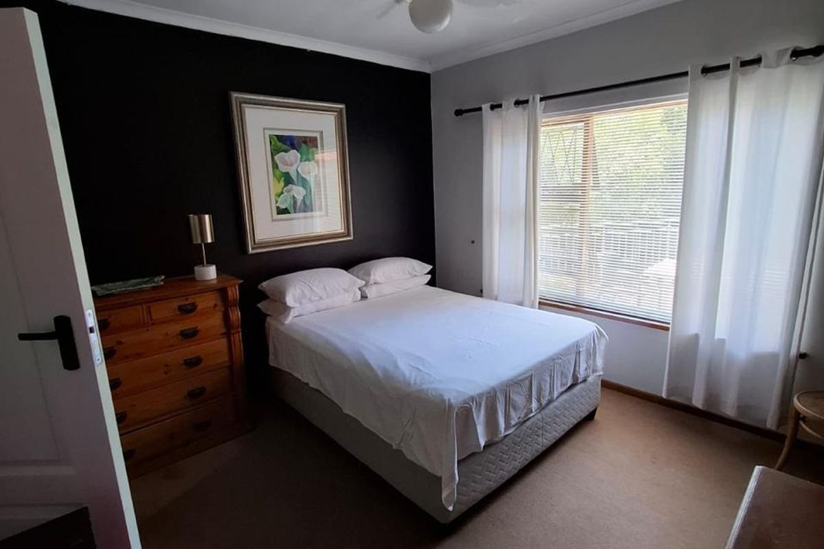 A well-lit bedroom featuring a ceiling fan, carpeted flooring, and a large window with fitted blinds.