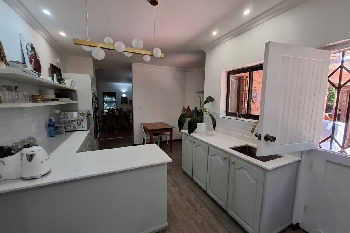 A bright, modern kitchen featuring light-toned cabinetry, quartz countertops, a functional dutch door, and open shelving, creating a clean and inviting culinary space.