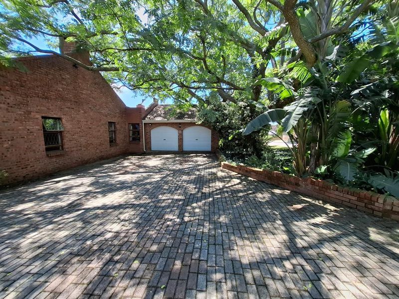 Front exterior view of the property featuring a brick driveway, double garage, and mature landscaping.