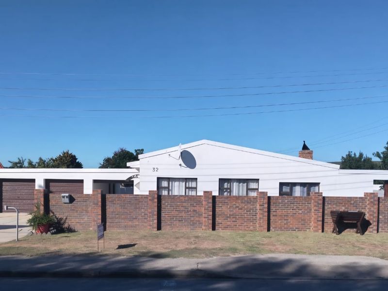 Front elevation of a single-story house featuring a brick boundary wall, driveway, and garage access.