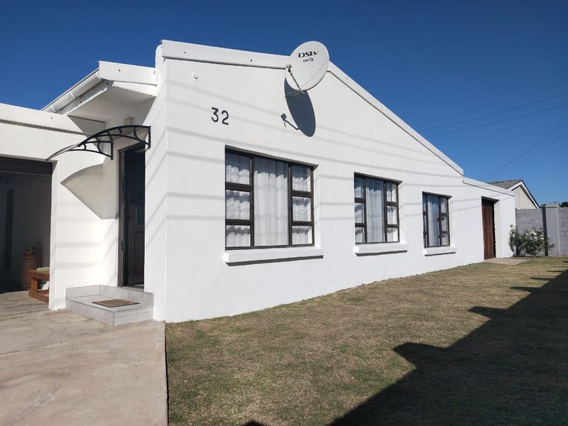 Front elevation of a white-painted house featuring aluminium window frames, a concrete driveway, and a satellite dish mounted on the exterior wall.