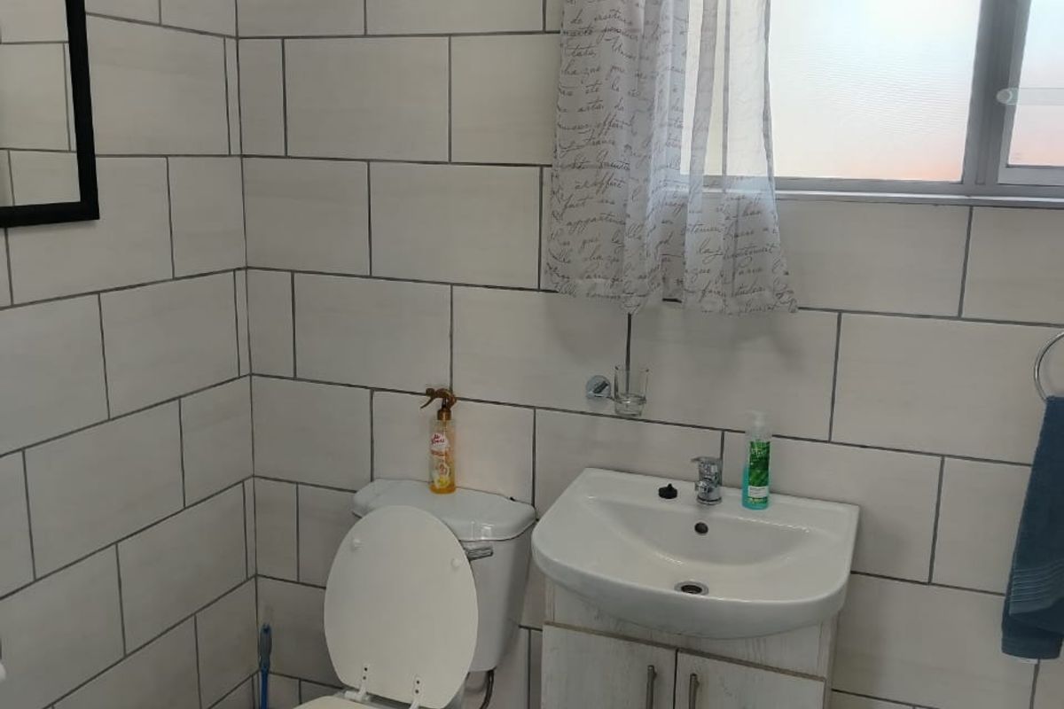 A functional bathroom featuring a wall-mounted vanity with basin, toilet, and full-height wall tiling.