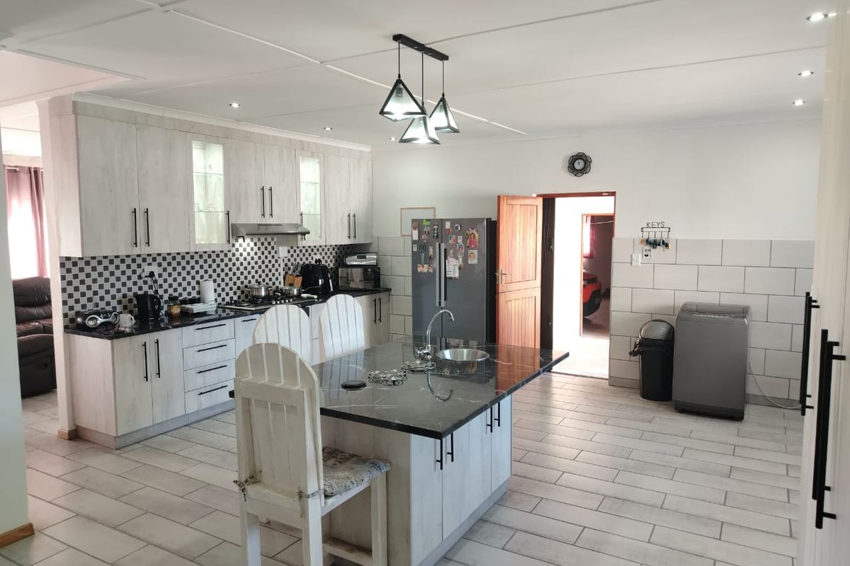 Modern kitchen featuring a central island with a sink, light-toned cabinetry, tiled backsplash, and integrated appliances, offering a functional and well-lit cooking space.
