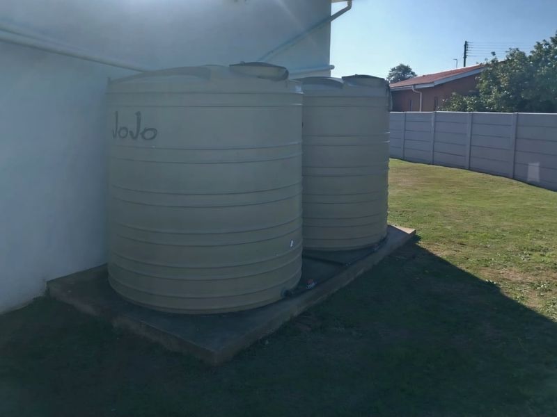 Two large plastic water storage tanks positioned on a concrete base against the exterior wall of the property.