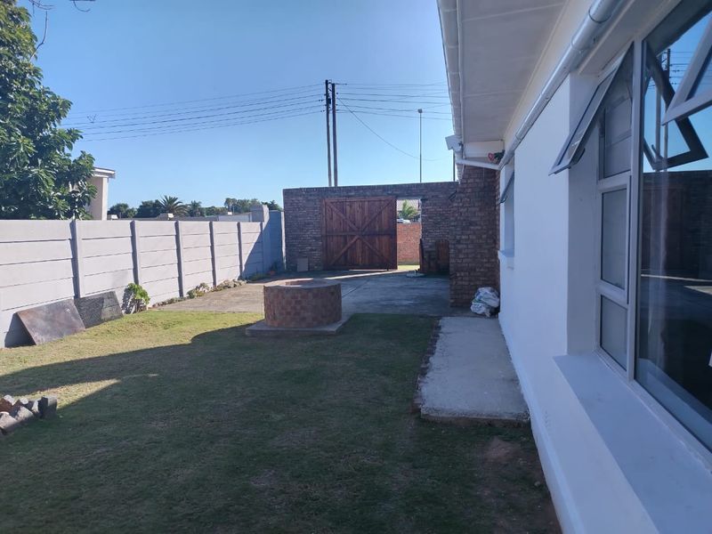Rear garden area featuring a lawn, brick fire pit, concrete paving, and a secure boundary wall with a wooden gate.