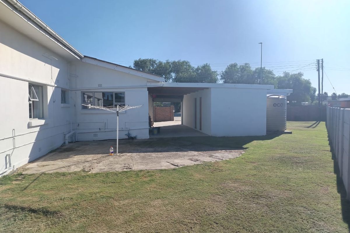 Rear exterior view of the property featuring a concrete patio area, carport, and a water tank set within a grassed backyard.