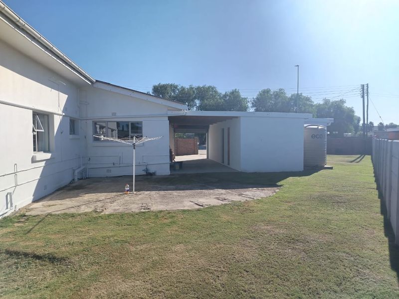 Rear exterior view of the property featuring a concrete patio area, carport, and a water tank set within a grassed backyard.