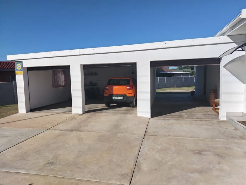 A three-bay open-front garage structure with a concrete driveway and white painted exterior walls.
