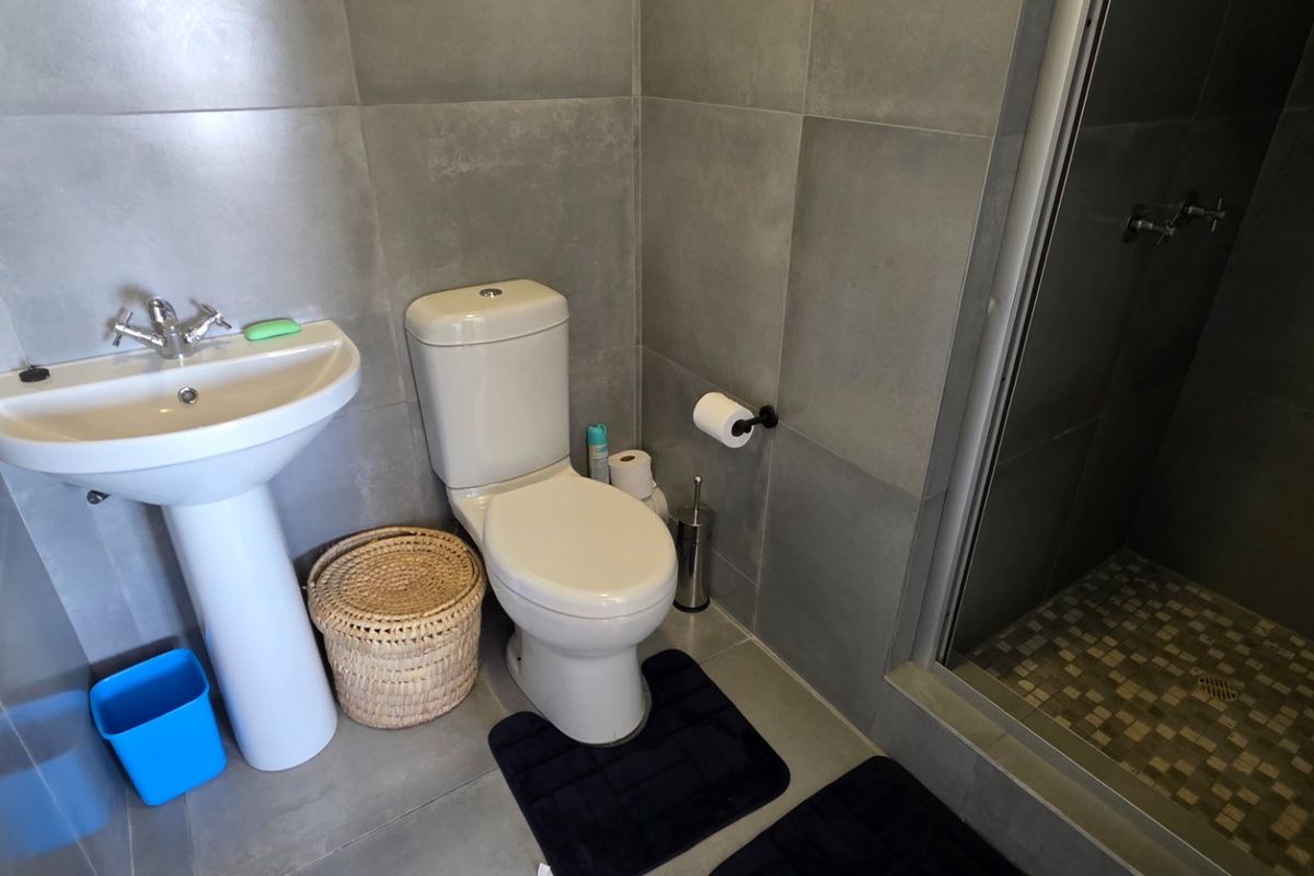 Modern bathroom featuring grey wall tiles, a pedestal basin, a toilet, and a glass-enclosed shower with mosaic floor tiling.