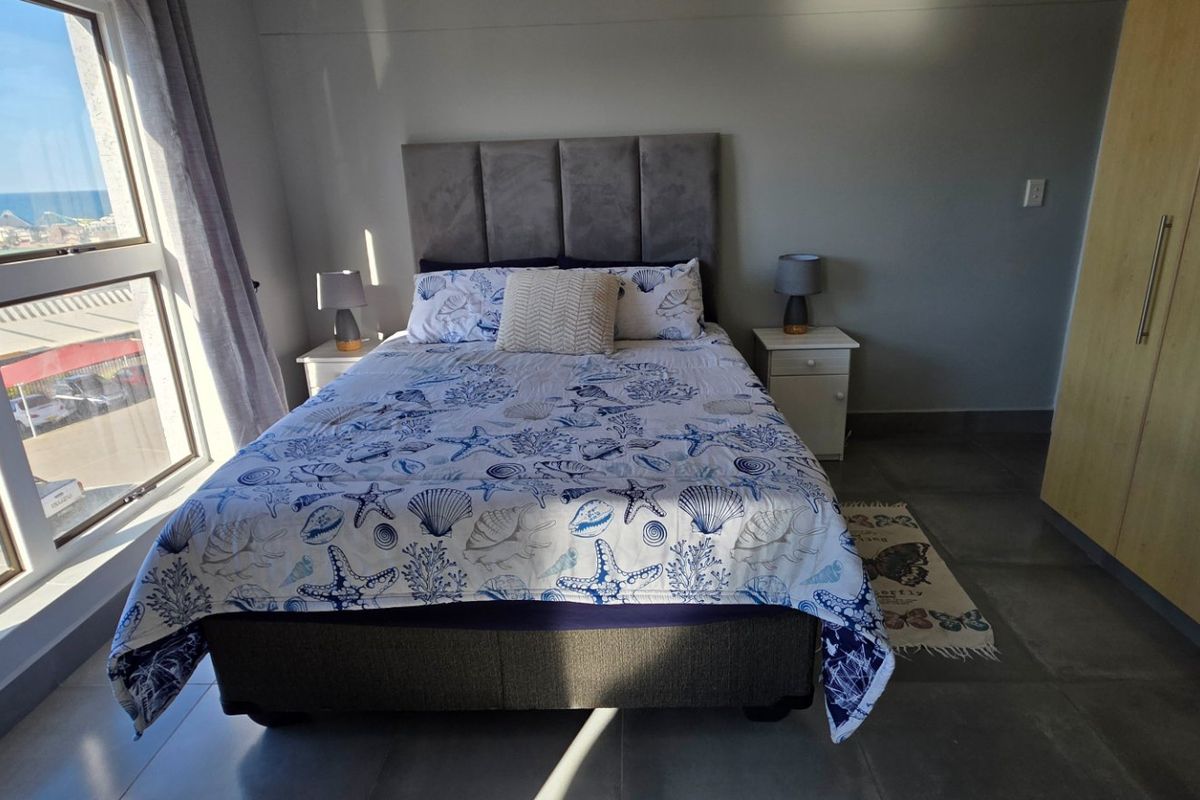 A bright bedroom featuring large windows with coastal views, neutral tiled flooring, and ample built-in cupboard storage.