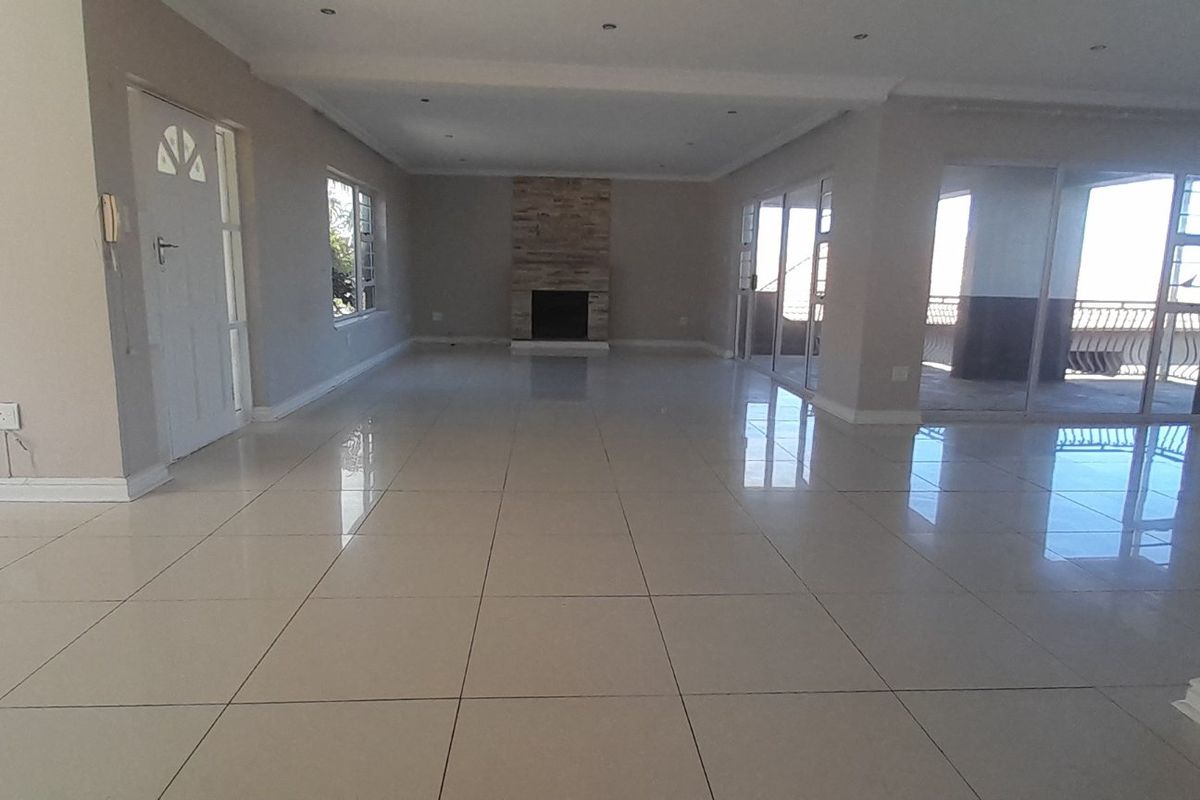 Spacious, open-plan living area featuring polished porcelain floor tiles, a stone-clad fireplace, and large sliding glass doors leading to an outdoor space.