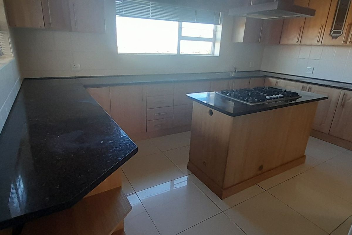 Spacious kitchen featuring wooden cabinetry, granite countertops, a central island with a gas hob, and tiled flooring.