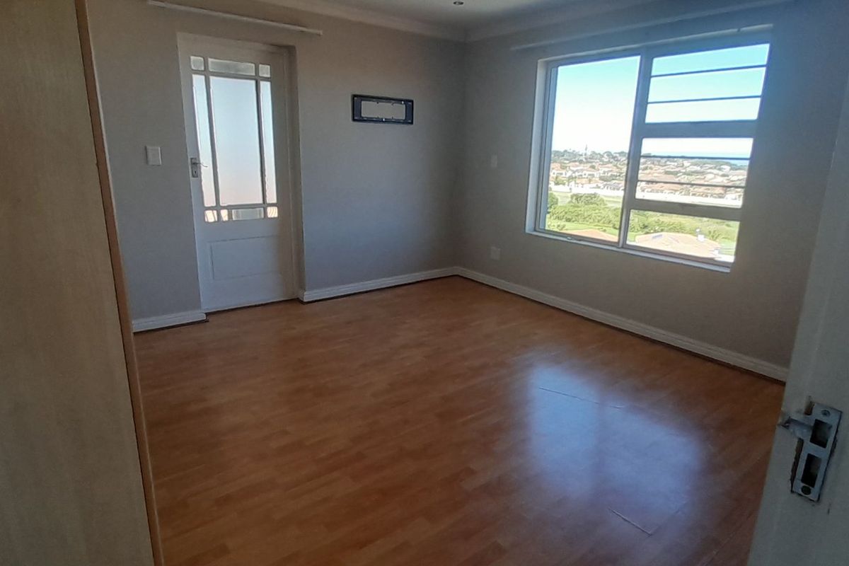 A bright, empty bedroom featuring laminate flooring, neutral walls, and a large window offering natural light and exterior views.