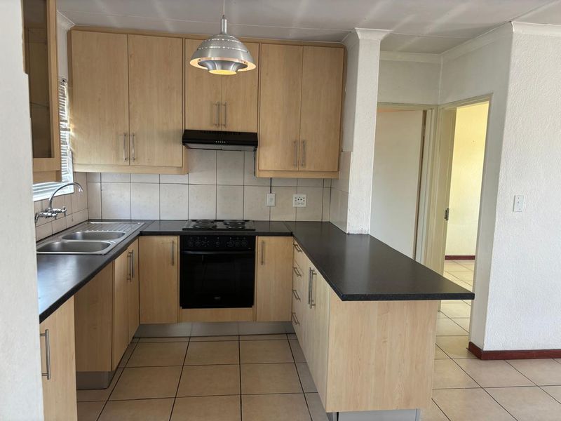 A functional kitchen featuring light-wood cabinetry, dark countertops, built-in oven with hob, and tiled flooring, offering a clean and practical workspace.