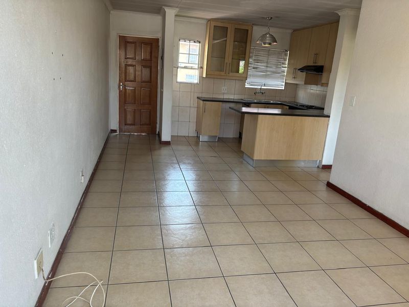 An open-plan living and kitchen area featuring tiled flooring, light wood cabinetry, and a functional layout, currently presented as a vacant space.
