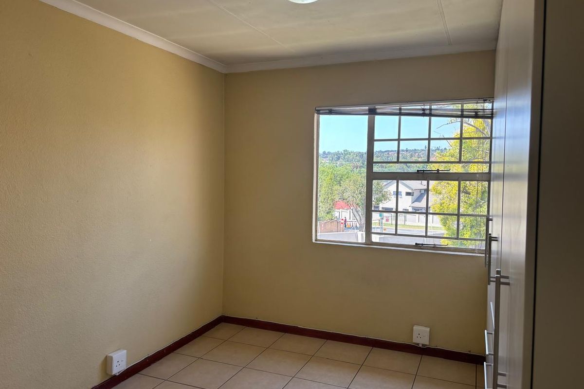 An empty bedroom featuring tiled flooring, a built-in wardrobe, and a window with security bars, offering a functional space ready for personalization.