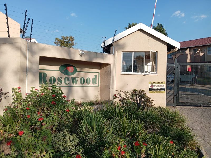 The entrance to Rosewood apartment complex featuring a security guard house, perimeter wall with electric fencing, and a controlled access gate.