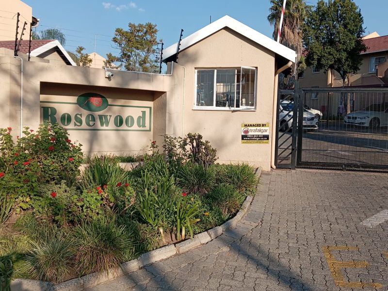 The entrance to Rosewood apartment complex featuring a guard house, security gate, electric fencing, and paved driveway access.