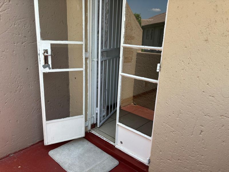 A small balcony or patio area featuring a metal security gate and glass door, with visible wear on the floor and door frame finishes.