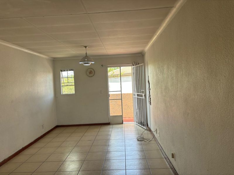 An empty living room featuring tiled flooring, a security gate leading to the exterior, and a simple pendant light fixture.