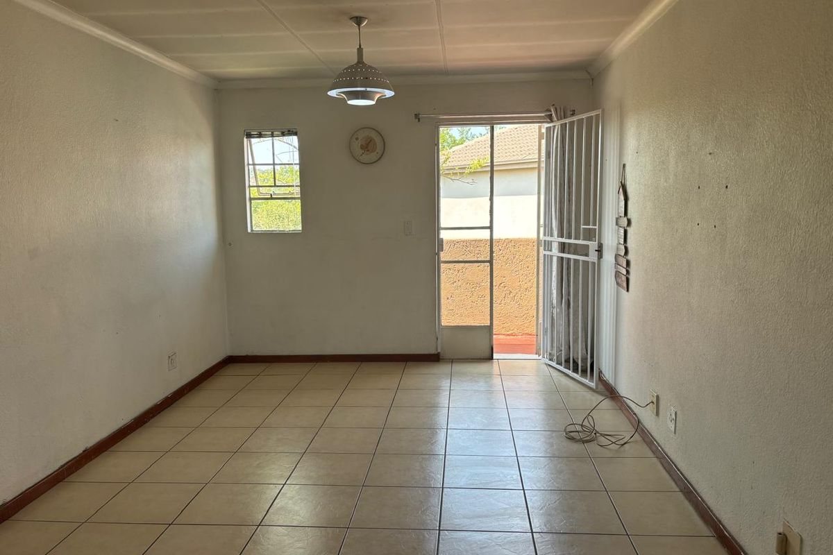 An empty living room featuring tiled flooring, a security gate leading to the exterior, and a central pendant light fixture.