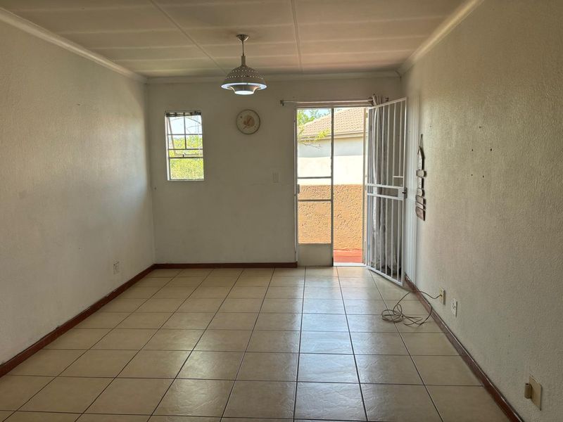An empty living room featuring tiled flooring, a security gate leading to the exterior, and a central pendant light fixture.