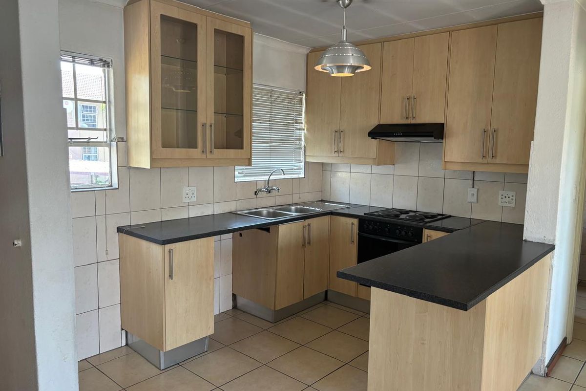 A functional kitchen featuring light wood-finish cabinetry, dark countertops, built-in oven and hob, and tiled flooring, offering a clean and practical workspace.