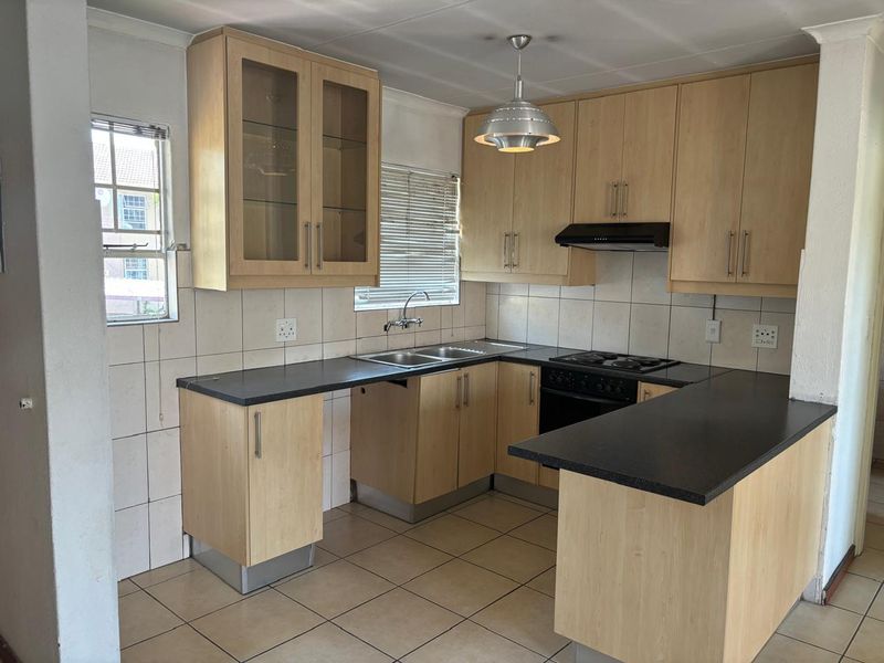 A functional kitchen featuring light wood-finish cabinetry, dark countertops, built-in oven and hob, and tiled flooring, offering a clean and practical workspace.