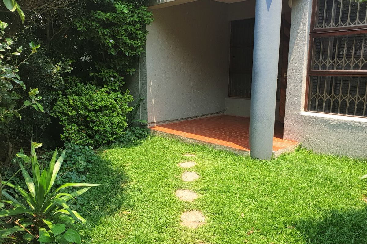 A private ground floor patio area featuring tiled flooring, a structural concrete column, and direct access to a small garden space.