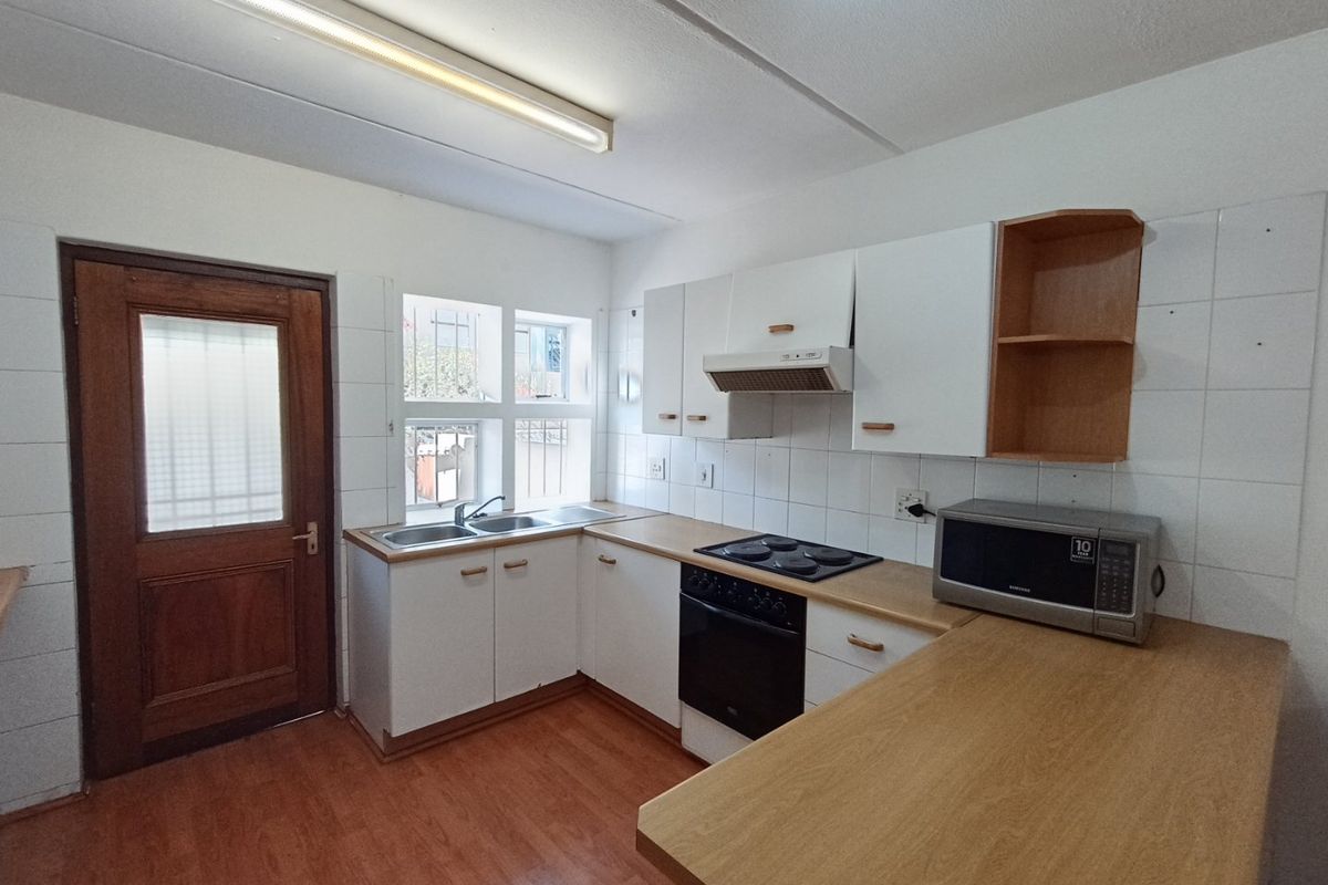 A functional kitchen featuring white cabinetry, laminate countertops, a double basin sink, and built-in cooking appliances with a tiled splashback.