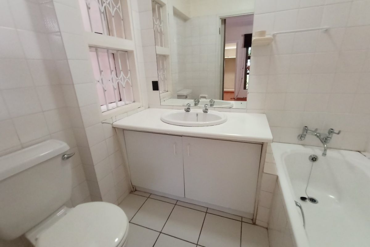A functional bathroom featuring a vanity cabinet with basin, bathtub, toilet, and tiled finishes, offering a clean and neutral space ready for updates.