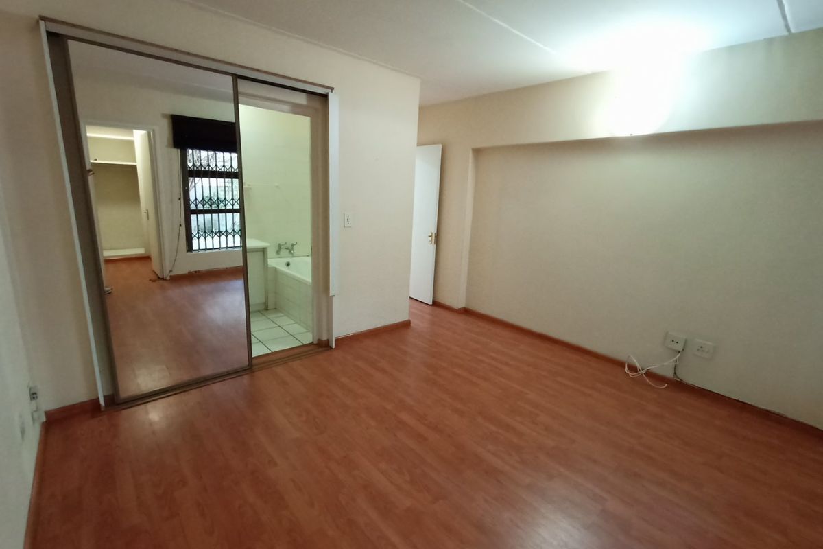 A spacious bedroom featuring laminate flooring and a large built-in mirrored wardrobe, with direct access to an en-suite bathroom.