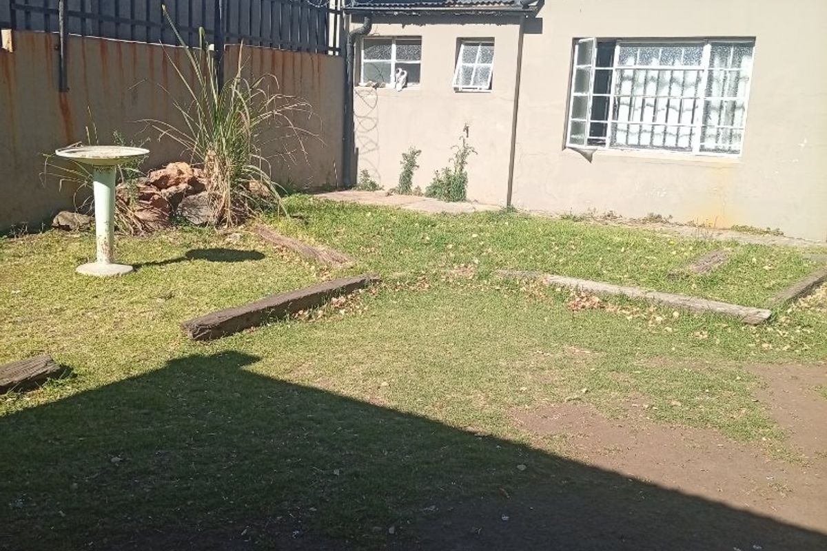 Rear garden area featuring a concrete boundary wall with razor wire, security-barred windows, and basic lawn landscaping.