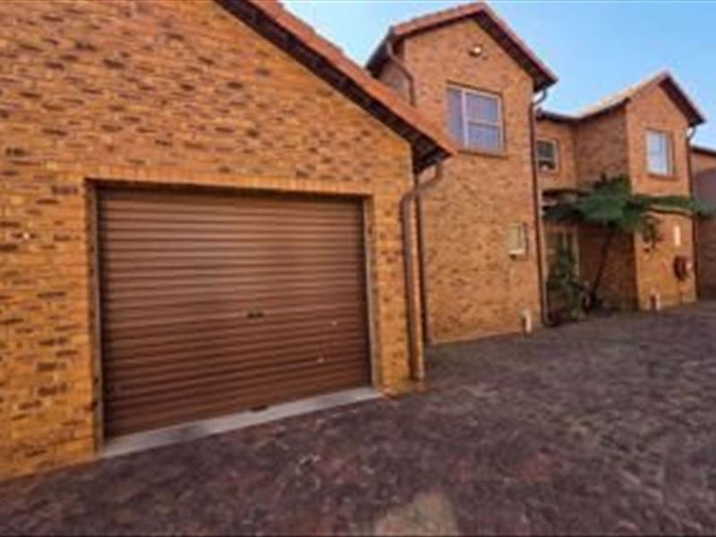 Front exterior view of a double-story townhouse featuring a face brick facade, a roll-up garage door, and a paved driveway.