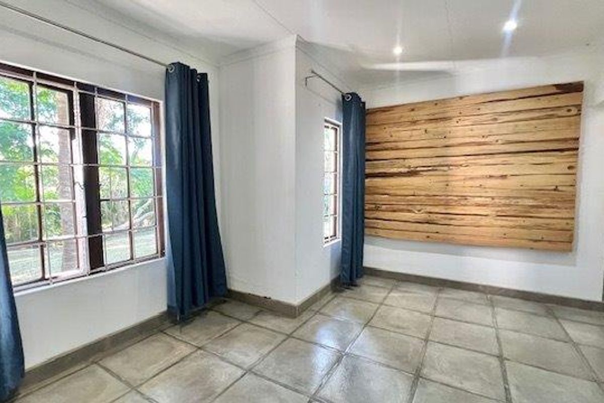 A bright, empty living area featuring neutral tiled flooring, recessed lighting, and a decorative timber-clad feature wall.