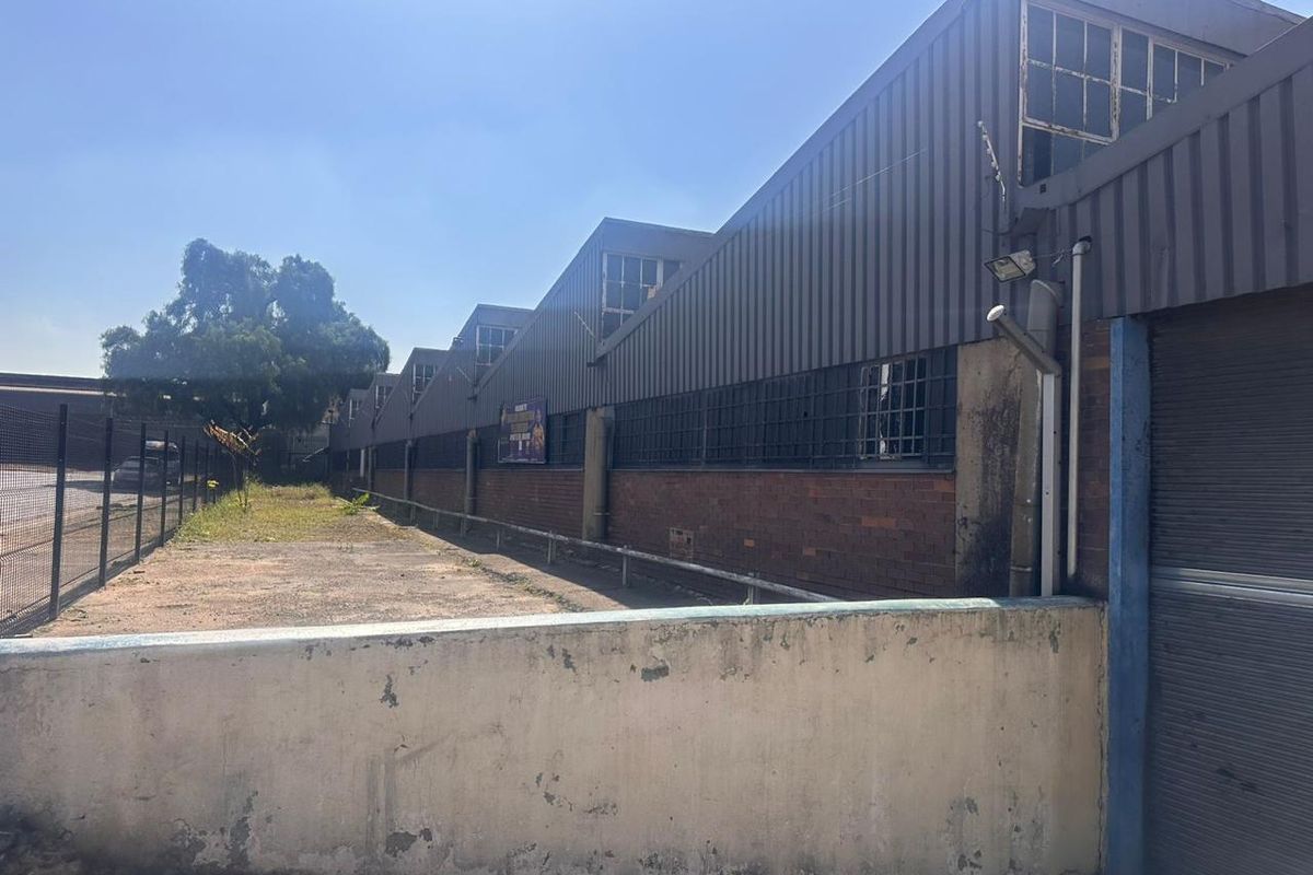 Rear exterior view of an industrial warehouse facility featuring corrugated metal cladding, brick masonry, and a secure perimeter boundary wall.