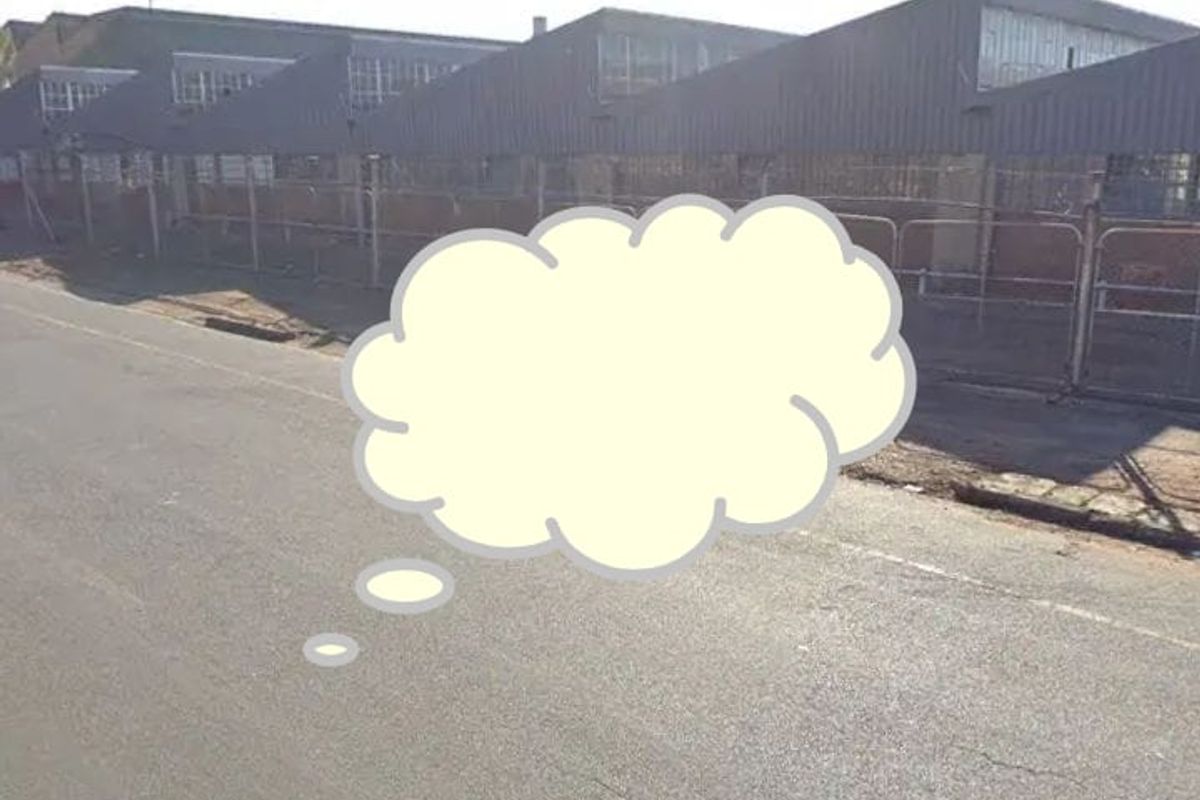 Street view of an industrial property featuring a sawtooth roof design and metal cladding, enclosed by perimeter chain link fencing.