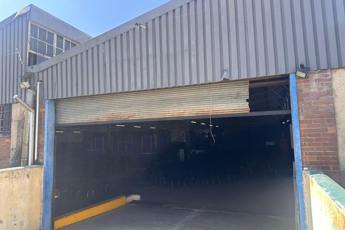 Commercial warehouse exterior featuring a large roller shutter door entrance, corrugated metal cladding, and a concrete access ramp.