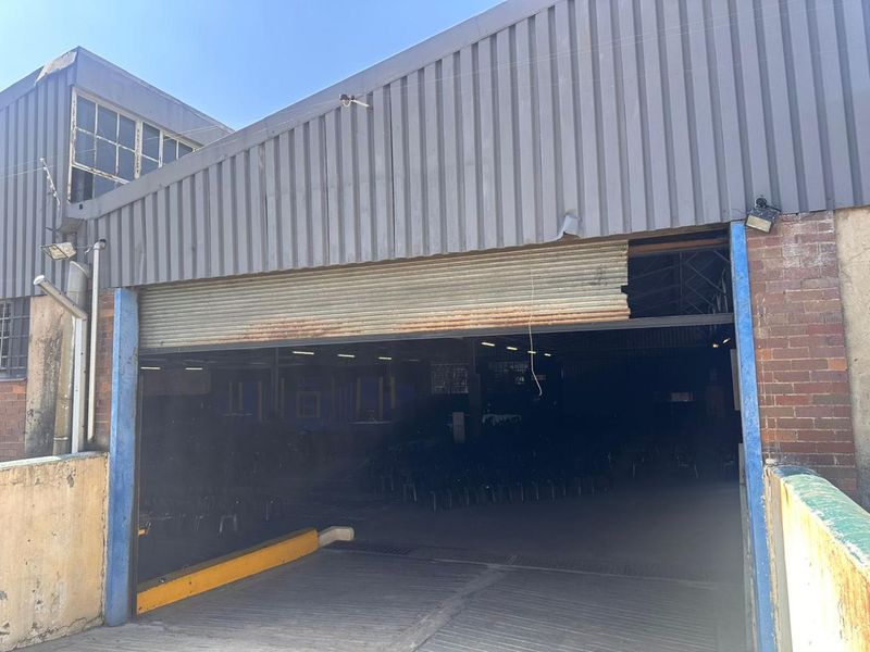 Commercial warehouse exterior featuring a large roller shutter door entrance, corrugated metal cladding, and a concrete access ramp.