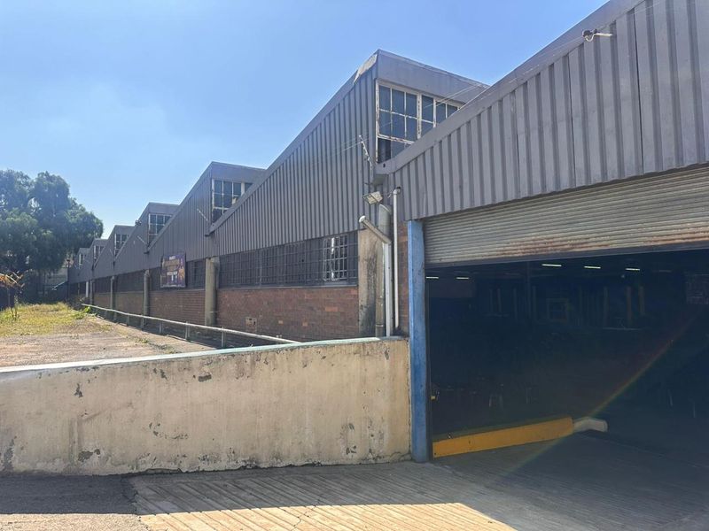 Exterior view of a commercial warehouse facility featuring a corrugated metal roof, brick facade, and a large roller shutter door entrance.