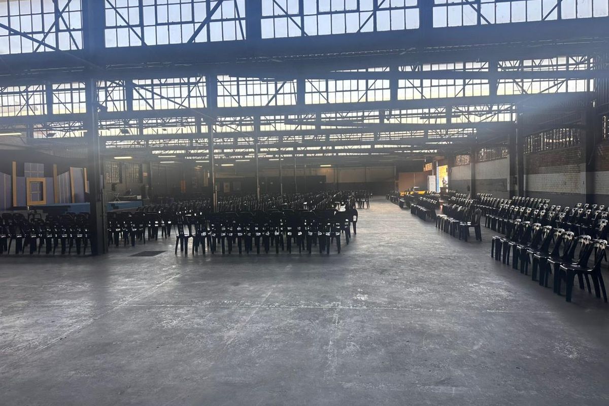 Expansive industrial open-plan commercial space featuring high ceilings with steel trusses, clerestory windows, and durable concrete flooring, suitable for various event or warehouse uses.
