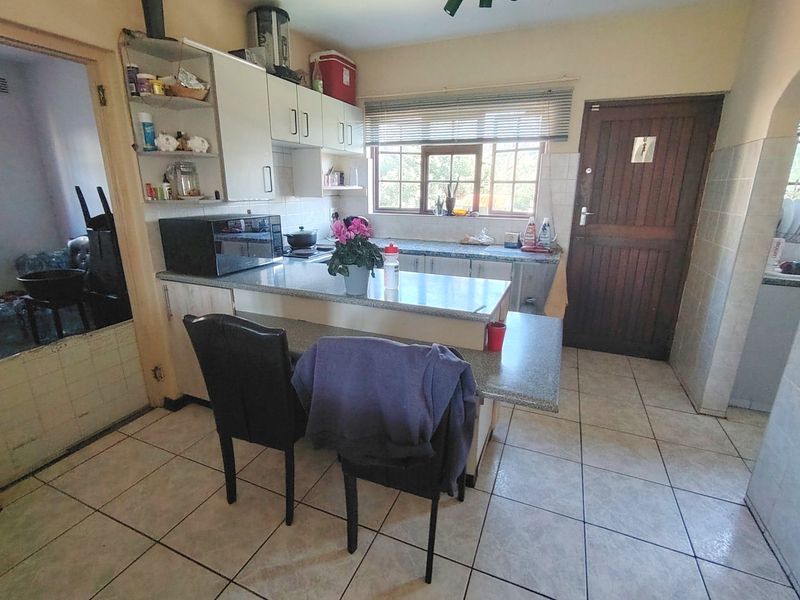 A functional kitchen featuring built-in cabinetry, laminate countertops, tiled flooring, and a timber door leading to the exterior.