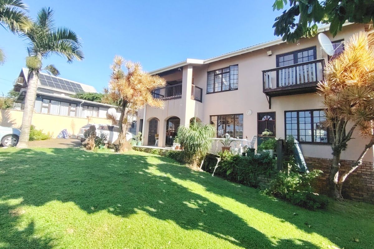 Rear view of a two-story residential property featuring a spacious lawn, upper-level balconies, and multi-pane windows.