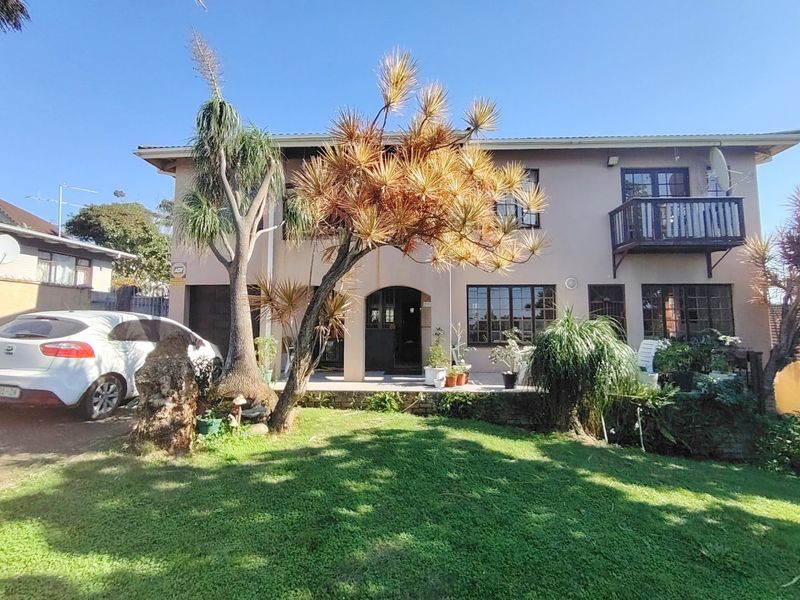 Front elevation of a two-story residential house featuring a lawn, driveway, and an upper-level balcony.