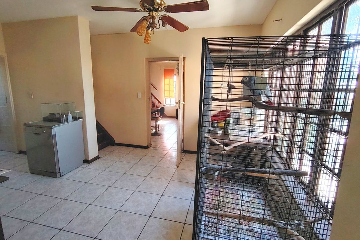 A living area featuring tiled flooring, a ceiling fan, and large windows, providing access to an adjacent room.