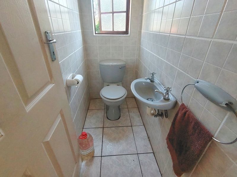 A compact guest bathroom featuring tiled walls and flooring, a wall-mounted basin, and a standard toilet.