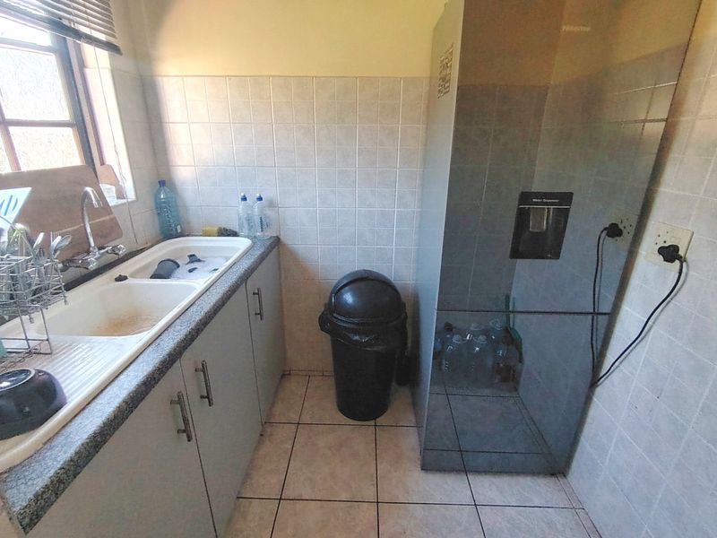 A functional scullery area featuring a double basin sink, tiled splashback, and built-in cabinetry, providing additional utility space for the home.