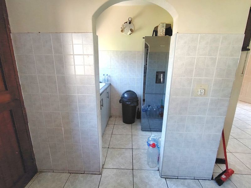 A functional scullery area featuring tiled walls and flooring, built-in cabinetry, and a sink, accessible through a classic arched doorway.