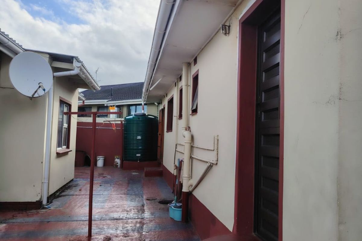 Rear exterior view of the property featuring a paved courtyard, concrete steps, and a water storage tank.